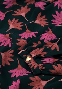 Bloemenstof met een donkergroene achtergrond, met roze en oranje bloemen. Inclusief een gouden hartvormige knop met het detail "Chante".