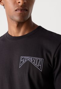 Black short-sleeve t-shirt made of cotton, featuring a white graphic logo on the chest. Smooth texture with a crew neckline.
