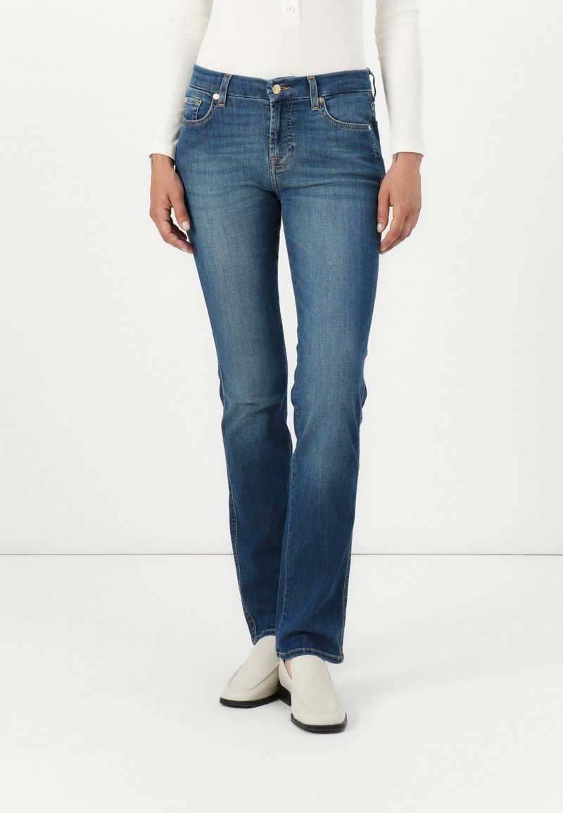 Blue denim jeans with a straight-leg design, five pockets, subtle stitching, and a button closure at the waistband. Paired with white shoes.
