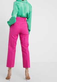 Satin grön långärmad blus kombinerad med högmidjade, korta rosa byxor och genomskinliga klackar, som visar upp släta texturer och klara färger.
