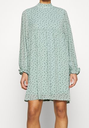 Lysegrøn kjole med høj halsudskæring, lange ærmer og en indsnævret talje. Har et blomsterprintmønster over hele. Fremstillet af blødt stof.