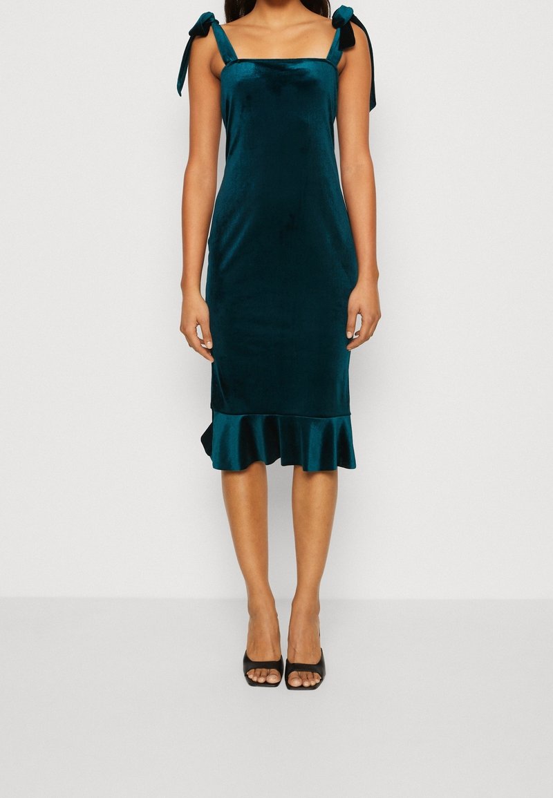 Teal sammetklänning med axelband, figurnära liv och volangkant. Slät yta med en lätt glans och minimalistisk design.