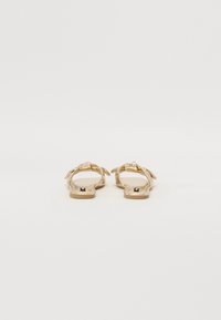 Gull sandaler med flat såle i gull, med et vevd stroppdesign, åpen bak og flat såle. Har en glatt tekstur og minimalistisk maskinvare.