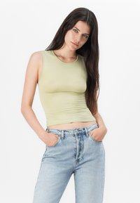 Light green sleeveless top made of stretchy material, fitted design, with a round neckline paired with high-waisted light blue denim jeans.