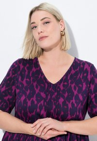 Abito con stampa leopardata viola e nera, maniche corte e scollo a V. Il tessuto appare a costine con pieghe lungo la parte anteriore.