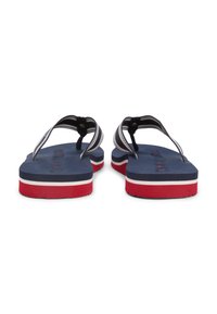 Μπλε σκούρες σαγιονάρες με παχιές λαστιχένιες σόλες, κόκκινες και λευκές λεπτομέρειες, και μαύρα υφασμάτινα λουριά με λευκές ρίγες και ανάγλυφο πέλμα.