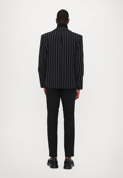 Black and white striped blazer with padded shoulders, paired with black slim-fit trousers and black shoes. Plain background.