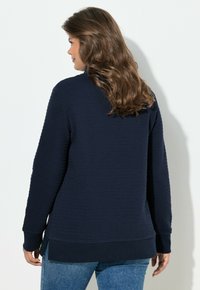 Sudadera azul marino con textura, cuello redondo, mangas largas y dobladillo acanalado. Cuenta con aberturas laterales para facilitar el movimiento.