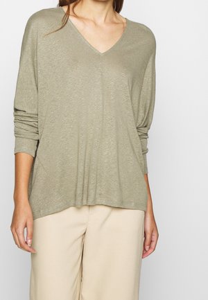 Haut à manches longues à col en V de couleur vert olive, fabriqué en tissu léger avec une coupe décontractée, associé à un pantalon beige clair.