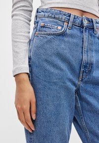 Jeansy z wysokim stanem w niebieskim deni czy, charakteryzujące się klasycznym pięciopocketowym fasonem, miedzianymi nitami oraz lekko przetartym wykończeniem z subtelną fakturą.