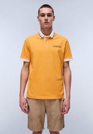 Orange polo-shirt med en hvid og maroonstribet krave, korte ærmer og broderet logo på brystet, parret med beige shorts.