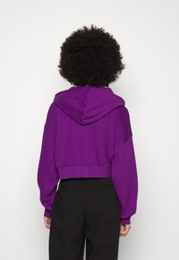 Sweatshirt corto viola con cappuccio, caratterizzato da maniche ampie e orlo a coste. Tessuto morbido e strutturato. Nessun motivo visibile né accessori.