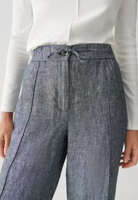 Lichte, grijze linnen broek met een elastische tailleband, koordsluiting en zijzakken. Heeft een gestructureerde, enigszins slibachtige stof.