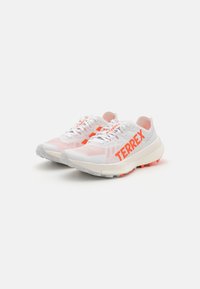 Scarpe da ginnastica bianche con accenti rosa e un logo "TERREX" arancione. Tomaia in mesh leggero, suola ammortizzata e suola testurizzata per una maggiore trazione.