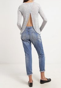 Graues langärmeliges Oberteil mit offenem Rücken, kombiniert mit hellblauen, leicht ausgefransten Jeans und schwarzen Ballerinas.