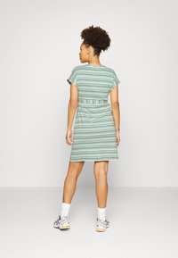 Vestido listrado em tons de verde com mangas curtas e cintura ajustada. Textura suave, até o joelho, usado com ténis desportivos e meias brancas.
