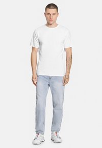 Biała koszulka z okrągłym dekoltem, krótki rękaw, w połączeniu z jasnoniebieskimi dżinsami, o luźnym kroju i lekkim przetarciu, noszona z szarymi trampkami.