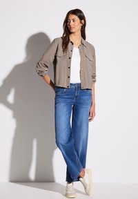 Veste courte gris clair avec fermeture à bouton, deux poches poitrine, associée à un jeans bleu décontracté et des baskets blanc cassé. Tissu lisse et décontracté.