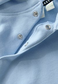 Jasnoniebieski ubranie z metalowymi zatrzaskami. Charakteryzuje się miękką fakturą i casualowym designem. Tkanina wydaje się gładka i lekka.