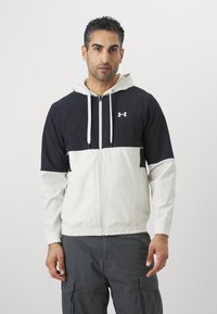 Giacca con cappuccio e zip nera e bianca. Tessuto morbido, polsini e orlo elasticizzati, con un logo sul petto. Vestibilità casual con un design bicolore.