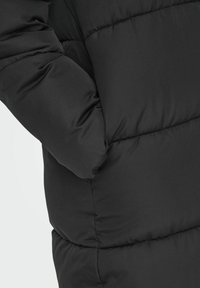 Veste doudoune noire avec un design matelassé, texture lisse et une poche sur le côté. Le matériau semble léger tout en étant isolant.