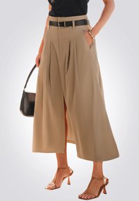 Pantalones de pierna ancha beige con pliegues, un cinturón negro y bolsillos laterales. Combinados con sandalias de tacón transparentes y un bolso negro.