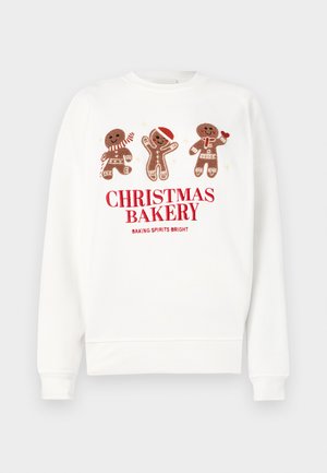 Bijela dukserica sa grafikom medenjaka u crvenim naglascima i natpisom "BOŽIĆNA PEKARA" u debelom crvenom slogu.