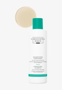 Bouteille de shampooing fortifiant avec un corps en plastique blanc et un capuchon turquoise, comportant un texte vert et noir. Au-dessus, un shampoing solide rond beige.