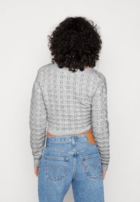 Szary, dziany krótki sweter o teksturowym wzorze, zestawiony z jasnoniebieskimi, wysokim stanem dżinsami z metką marki z tyłu.