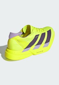 Neonowa żółta biega but z teksturowanym wierzchem, fioletowymi akcentami i masywną podeszwą LIGHTSTRIKE PRO. Posiada sznurówki i otwory wentylacyjne.