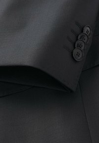 Polsino di giacca nera con una texture liscia, caratterizzato da quattro bottoni neri e cuciture dettagliate. Il tessuto presenta un motivo sottile.