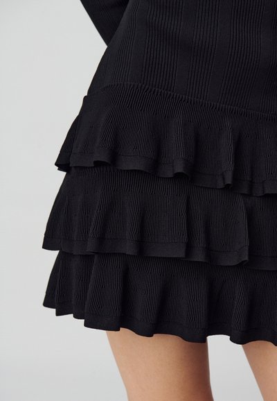 Abito nero a coste con multiple balze stratificate lungo l'orlo, con una superficie testurizzata e una vita elastica.