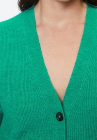 Cardigan de punto verde con diseño de cuello en V, botón negro, tejido texturizado y bordes acanalados en contraste. Vista en primer plano que muestra los detalles.