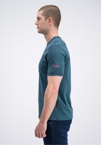 Medvilninis žalias žalsvas marškinėlis su apvalia apykakle, trumpomis rankovėmis ir etiketėle, siūta ant kairės rankovės. Lygios tekstūros.