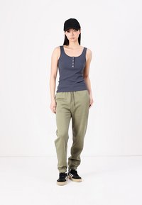 Sivá rebrovaná tielko s prednými gombíkmi, doplnené o mäkké olivové tepláky a čierne tenisky. Čierna čiapka dotvára outfit.