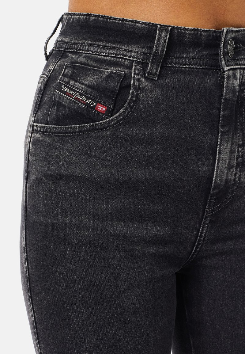 Jeans in denim nero con una texture sbiadita, dotati di una tasca frontale con un'etichetta di marca rossa e nera ben visibile, e chiusura con bottone metallico standard.