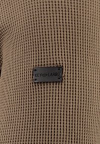 Tessuto di maglione rigato marrone con una superficie testurizzata, caratterizzato da un'etichetta rettangolare nera in rilievo con la scritta "KEY LARGO." Design testurizzato su tutta la superficie.