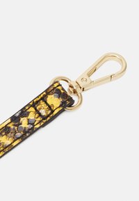Żółto-czarny skórzany pasek do breloczka z nadrukiem wężowej skóry, wyposażony w złoty metalowy karabińczyk i okrągły pierścień mocujący.