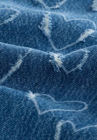 Denim tkanina u tamnoplavoj boji s istrošenom teksturom, s vezanim bijelim srcima raspršenim po cijeloj površini, stvarajući slojevit izgled.