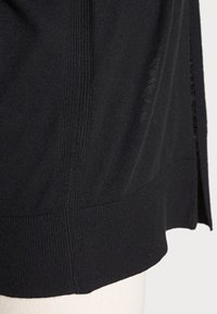 Top in maglia nera con texture a costine e orlo. Presenta aperture laterali per un tocco di dettaglio, con una finitura liscia sul fondo.