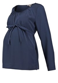 Blouse de maternité bleu marine à manches longues avec encolure arrondie et détail noué au-dessus du ventre.