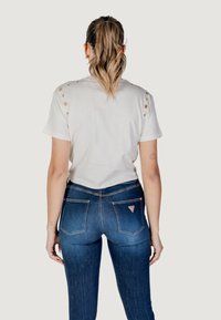 White t-shirt with shoulder eyelet details, paired with dark blue skinny jeans featuring a logo patch on the back pocket.