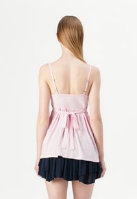 Pink cotton top with adjustable straps and a tied waist, paired with a layered navy blue ruffled skirt, viewed from the back.