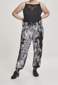 Femme portant un haut sans manches avec dentelle noire, un pantalon à motifs abstraits noir et blanc, et des baskets noires, se tenant avec les mains sur les hanches.