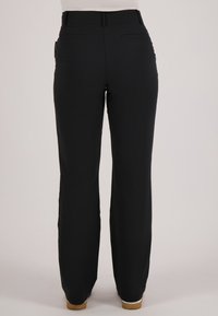 Persoon draagt zwarte high-waisted rechte broek en lichtbruine schoenen, staand tegen een effen lichte achtergrond.