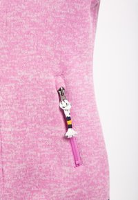Šviesiai rožinė fliso zip-up striukė su tekstūruotu raštu; turi užtrauktuką su dekoratyviu traukiamuoju elementu ir kontrastingos spalvos akcentu.