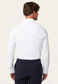 Witte langemouwen shirt met een klassieke kraag, een gladde textuur en knoopmanchetten, gecombineerd met marineblauwe broek met achterzakken.