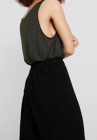 Top senza maniche verde scuro con una vestibilità comoda, abbinato a pantaloni larghi neri in tessuto testurizzato con vita elastica.