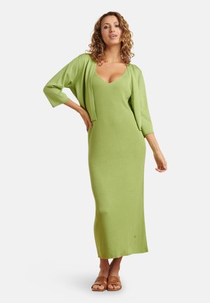 Ripp maxi Kleid in Hellgrün mit tiefem V-Ausschnitt und Dreiviertelärmeln. Kombiniert mit braunen Rutschsandalen, die eine entspannte Passform zeigen.