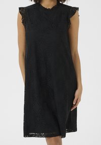 Černé krajkové šaty s květinovým vzorem, krátkými volánkovými rukávy a kulatým výstřihem. Texturovaná látka má složité výřezy.